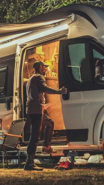 Motorhome RV Park Camping Caucasian Men and His Camper Van During Late Evening Hours. Motorhome RV Park Camping. Travel and Recreational Vehicles Theme.